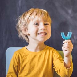 Little boy smiling and holding children’s sports mouthguard in Casper