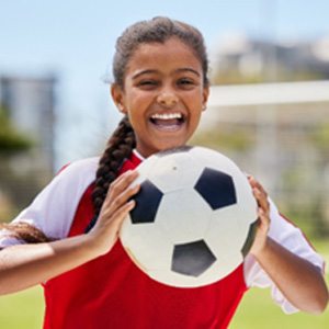 Young girl smiling while holding soccer ball on field