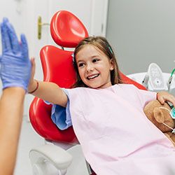 young girl sitting in dental chair high fiving dentist