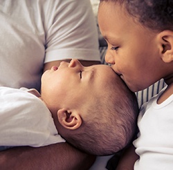 Older sibling kissing infant sibling on head