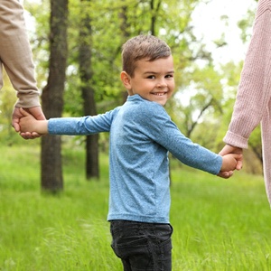 A young boy holding his parent’s hands and smiling after seeing a children’s dentist in Casper