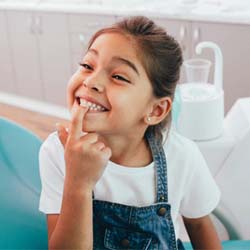 Smiling girl pointing to her tooth visiting Casper children’s emergency dentist