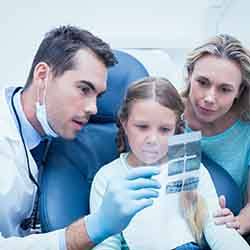 Dentist looking at child’s X-rays with mother nearby