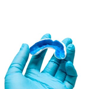 Dentist with blue gloves holding blue and white mouthguard