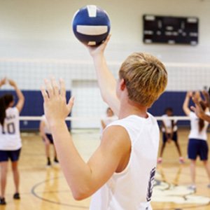 Teen with blonde hair serving volleyball in school gymnasium
