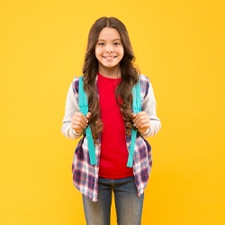 A young girl wearing a backpack and smiling after a positive dental cleaning in Casper