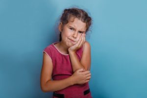 a little girl holding her cheek in pain