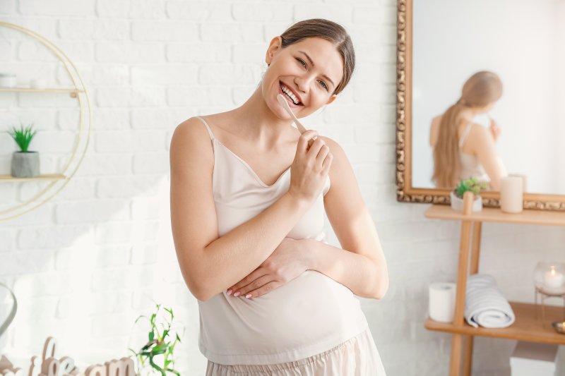 a young woman standing in her bathroom brushing her teeth while pregnant
