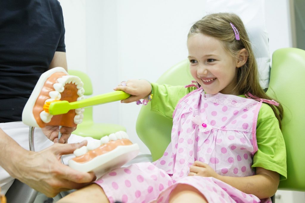 Child smiling while brushing oversized model of teeth