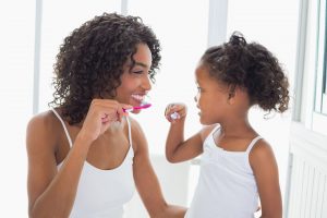 Woman and girl in white shirts brushing their teeth