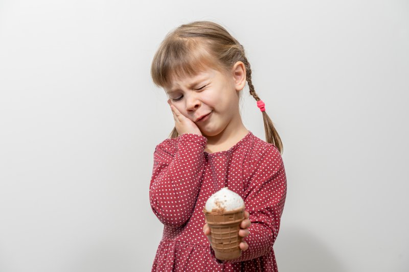 Child with ice cream holding their cheek due to tooth sensitivity