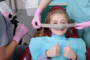 Child in patient’s chair giving a thumbs-up while receiving nitrous oxide